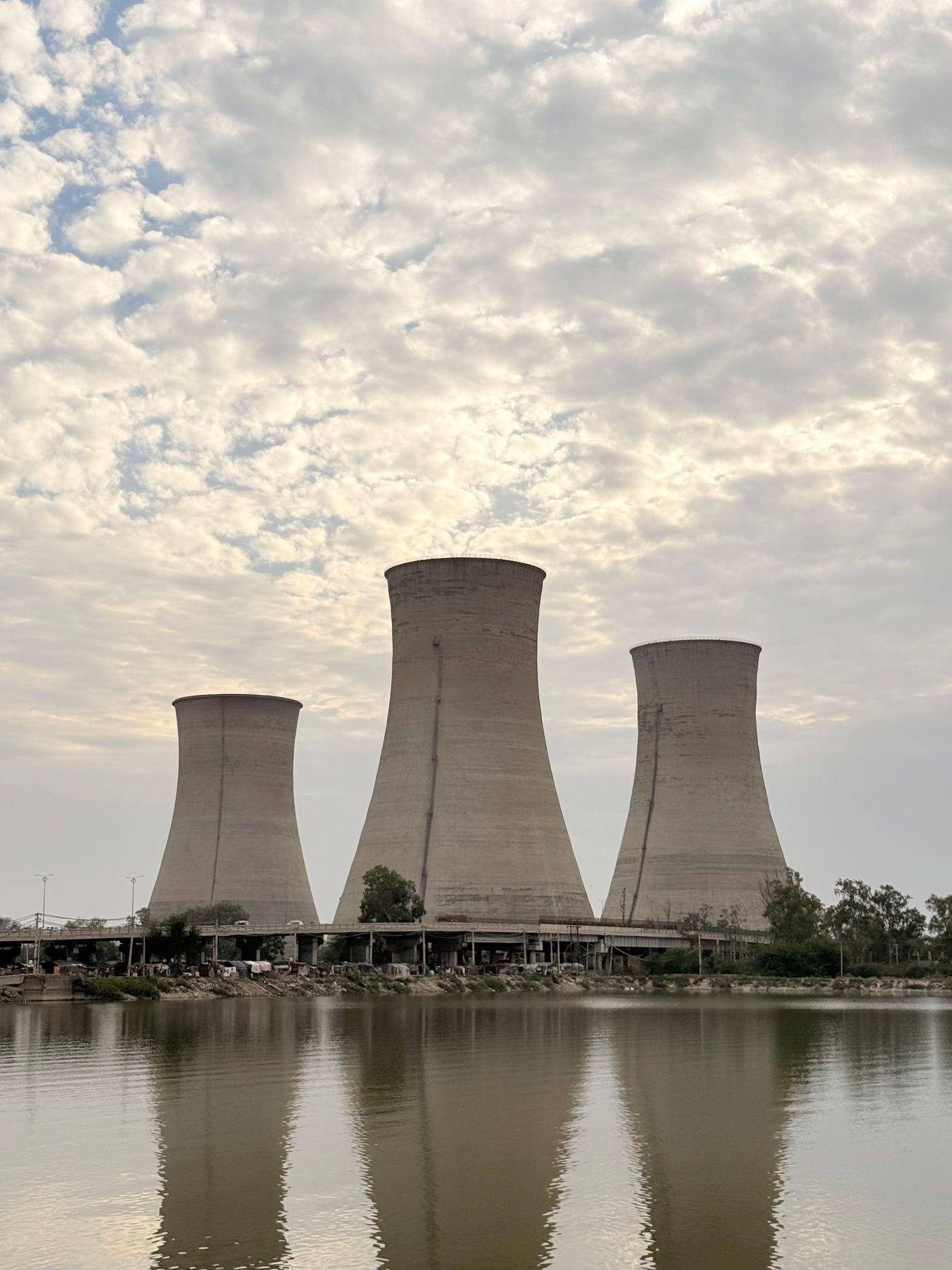 Industrial cooling towers reflected in the still water of a lake under a cloudy sky