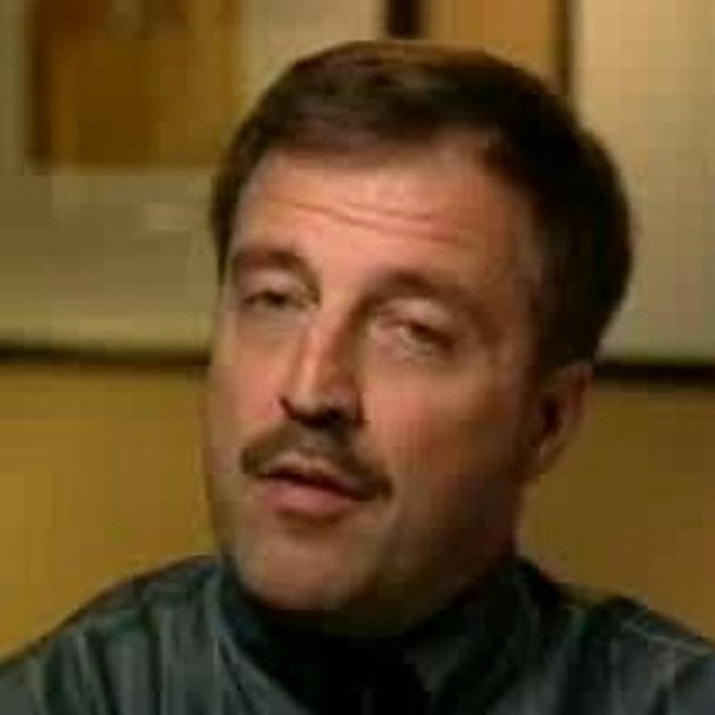 Dr Peter Moeller, in a dark collarless shirt, photographed indoors against a pale panelled wall during an interview